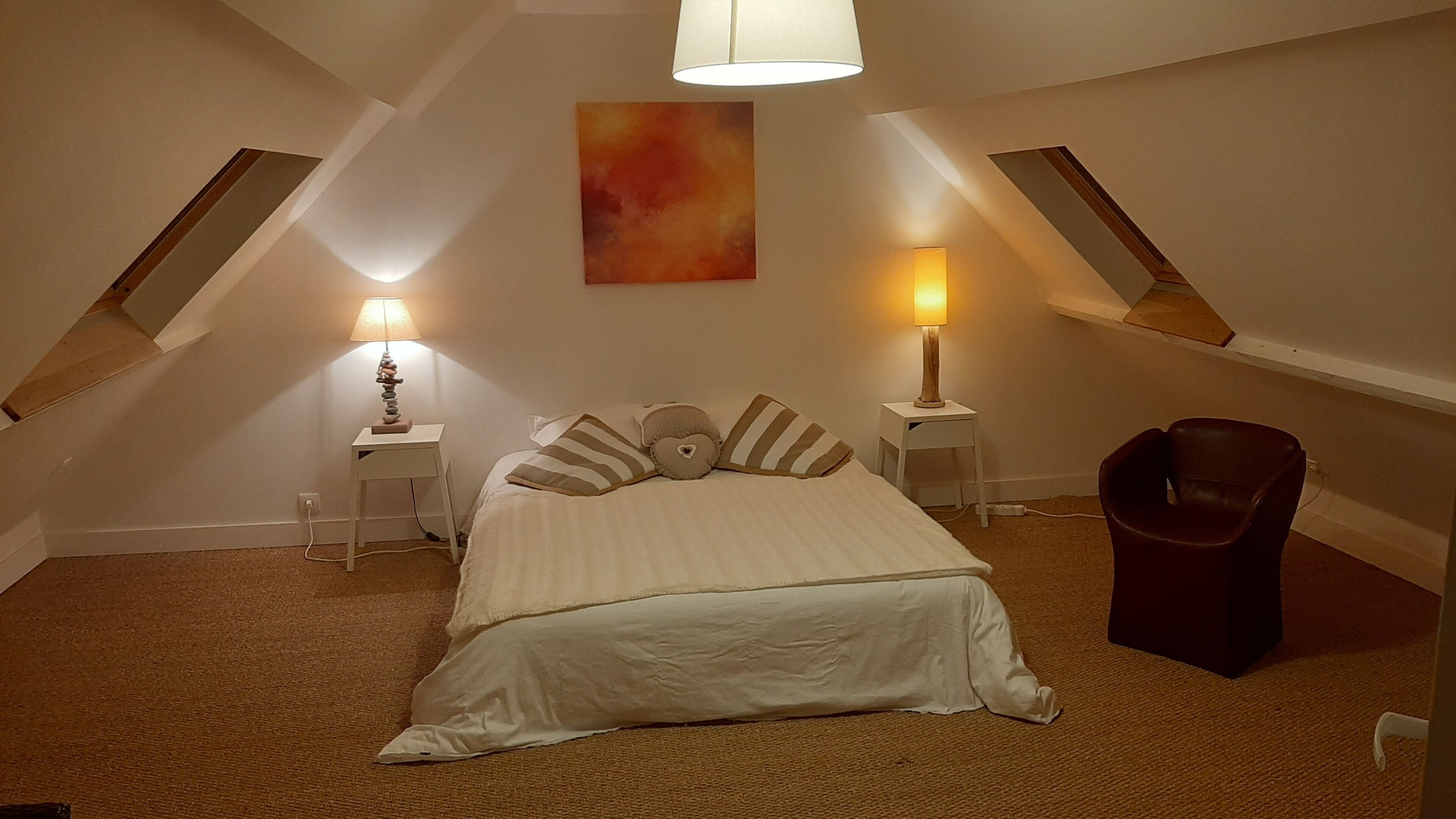 A bedroom with a bed, two bedside tables, a lamp on each table, a chair, and a painting on the wall.