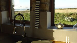 Una cocina con vista a la playa, una corbata a rayas colgada en la pared y un calentador de agua en el alféizar.
