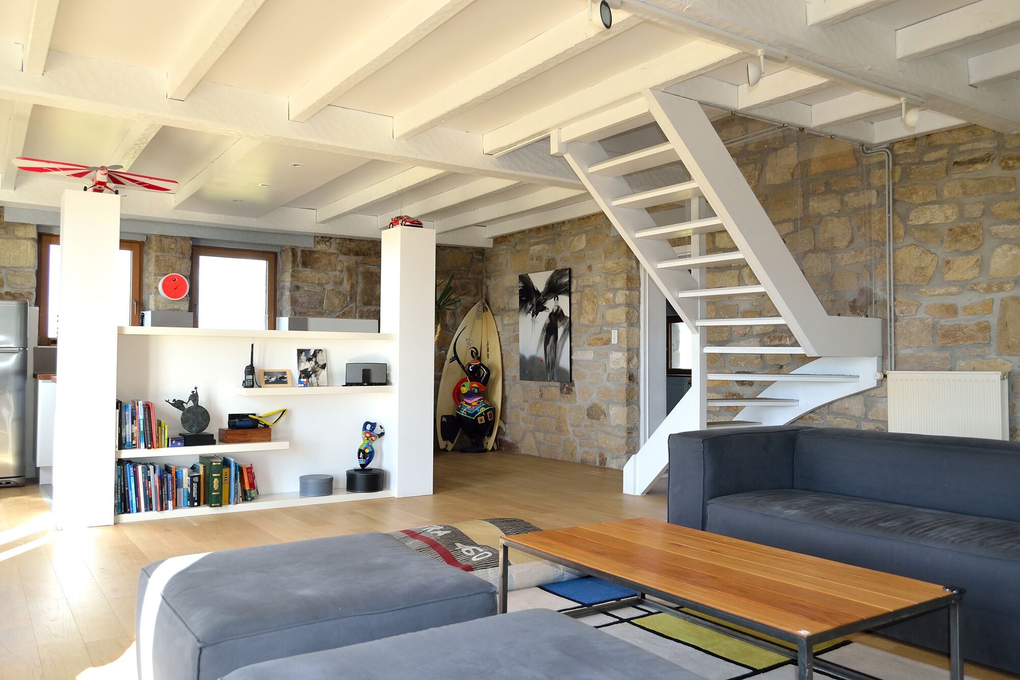 A modern living room with a staircase, a sofa, a coffee table, and a bookshelf.