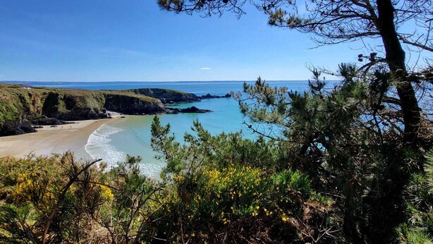 Paisaje costero con playa, aguas azul turquesa y montañas al fondo.