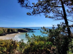 Un paysage côtier avec une plage, des eaux d’un bleu limpide et une chaîne de montagnes en arrière-plan.