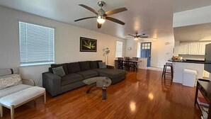 A spacious living area with a dark gray sectional sofa, a small coffee table, and a ceiling fan. - Hawaii Condo Close to Beach, Golf, Pool and Restaurants (Kapolei)