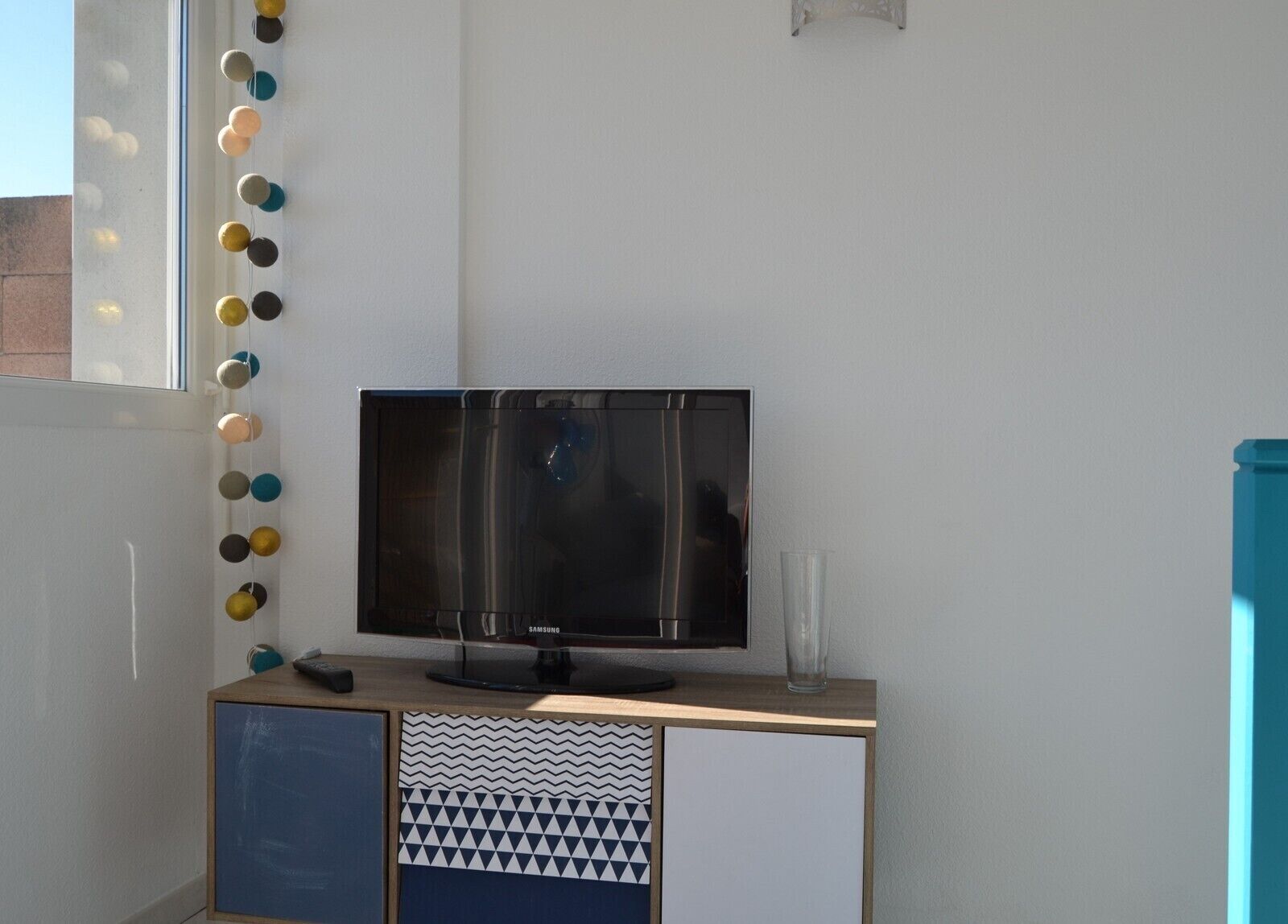 Uma TV Samsung sobre um móvel de madeira, com um armário decorado abaixo.