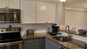 A kitchen with white cabinets, stainless steel appliances, a granite countertop, and a built-in dishwasher. - Surf Court 48- 1 Block To The Beach! (Hilton Head Island)
