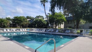 A swimming pool with a metal ladder, surrounded by a white fence, and shaded by trees. - Surf Court 48- 1 Block To The Beach! (Hilton Head Island)