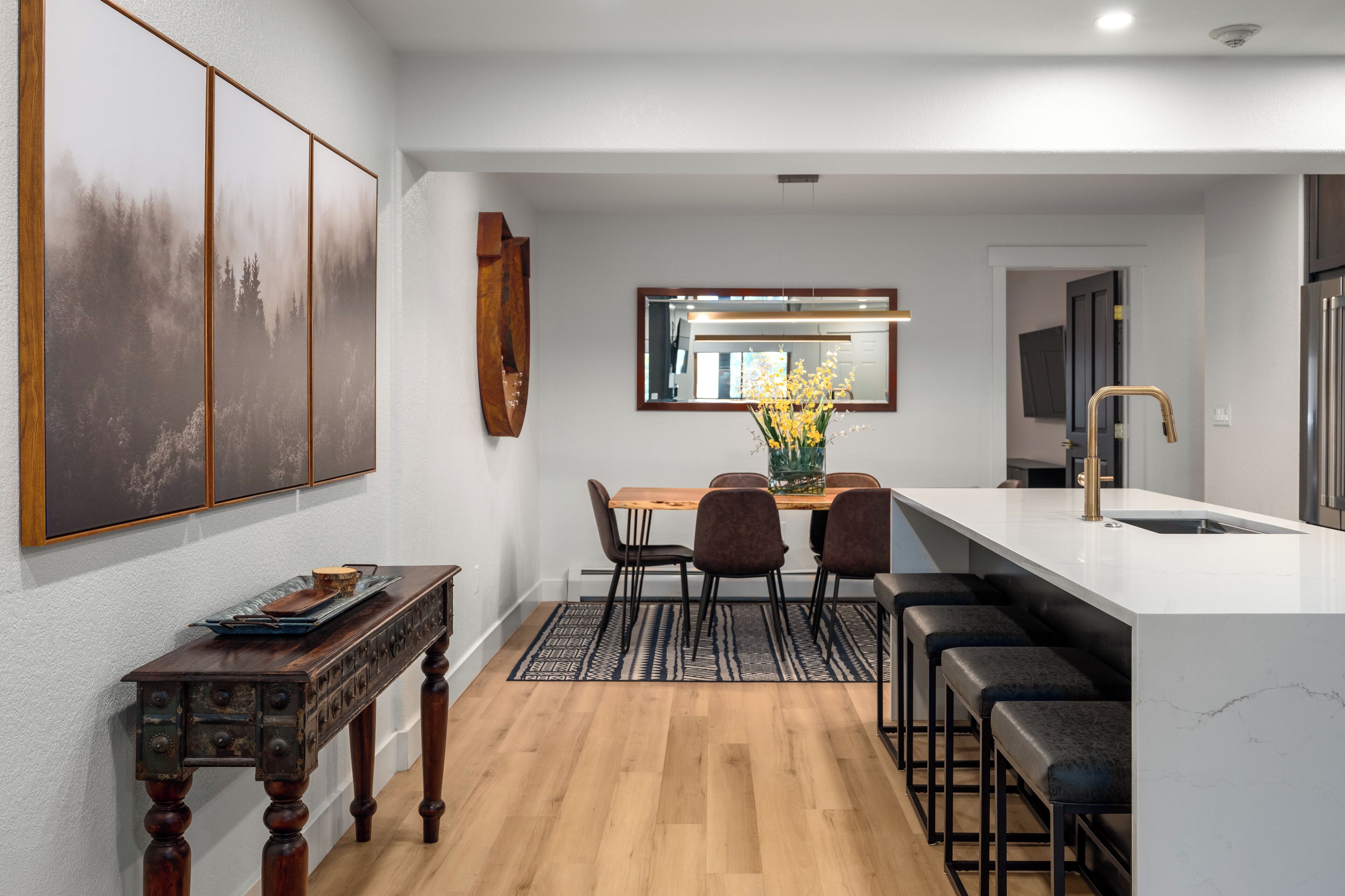 Une cuisine moderne dotée d’un îlot central, de tabourets de bar et d’un coin repas avec une table et des chaises en bois.