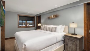 Une chambre avec un grand lit, une table de chevet avec une lampe, une fenêtre avec des stores et un élément décoratif fixé au mur.