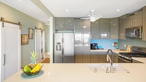 A modern kitchen with stainless steel appliances, a central island with a sink, and a ceiling fan. - Paradise Found | 2BR Condo | Ocean  Front Views | With AC (Kapaa)