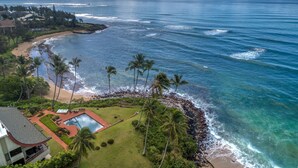 A beachfront property with a swimming pool, lush greenery, and a view of the ocean. - Paradise Found | 2BR Condo | Ocean  Front Views | With AC (Kapaa)