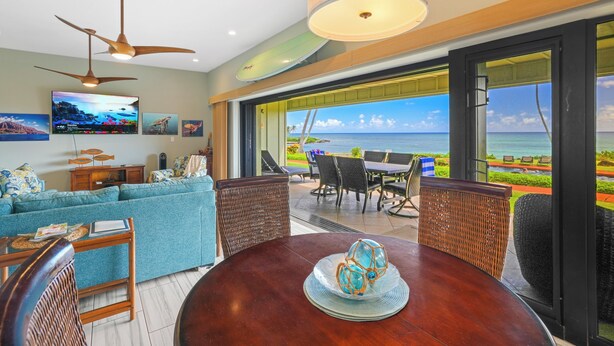 A modern living room with a large TV, comfortable seating, and a view of the ocean. - Paradise Found | 2BR Condo | Ocean  Front Views | With AC (Kapaa)