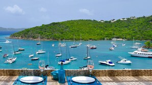 A marina with boats, a table set for two with a blue vase and wine glass, and a hillside in the background.