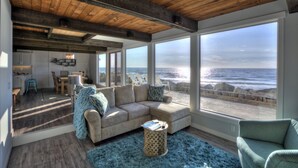 A spacious living room with a large window overlooking the ocean, a cozy seating area, and a wooden ceiling.
