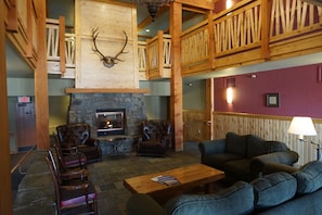 A lodge interior with a stone fireplace, leather armchairs, a sofa, and a wooden ceiling with antlers. - Incredible ski in ski out studio! Hot tub, underground parking,gym,rooftop deck, ski room!!! (Whitefish)
