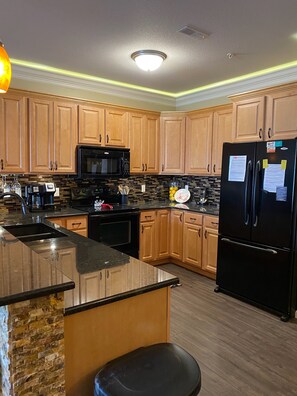 Enjoy cooking in this fully equipped kitchen with a sink, black faucet, refrigerator, microwave, and island with a barstool.