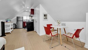 Eine moderne Küche mit einem Edelstahlkühlschrank, einem schwarzen Backofen und einer weißen Arbeitsplatte. Es gibt einen Essbereich mit einem weißen Tisch und roten Stühlen.