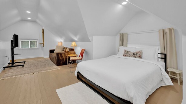 Ein geräumiges Schlafzimmer im Dachgeschoss mit einem großen Bett, einer gemütlichen Sitzecke und einem Flachbildfernseher.