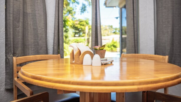 Een ronde houten tafel met vier stoelen, een zout- en peperstel in de vorm van een houten huis en een potplant op een tafelonderzetter.