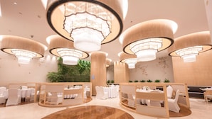 Un moderno vestíbulo de hotel con mesas redondas, sillas blancas y grandes candelabros.