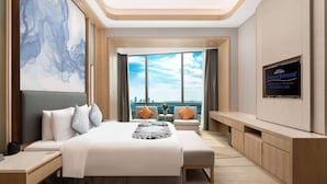 Una habitación de hotel moderna con una cama grande, televisor, vista a la ciudad y un cuadro abstracto de gran tamaño.