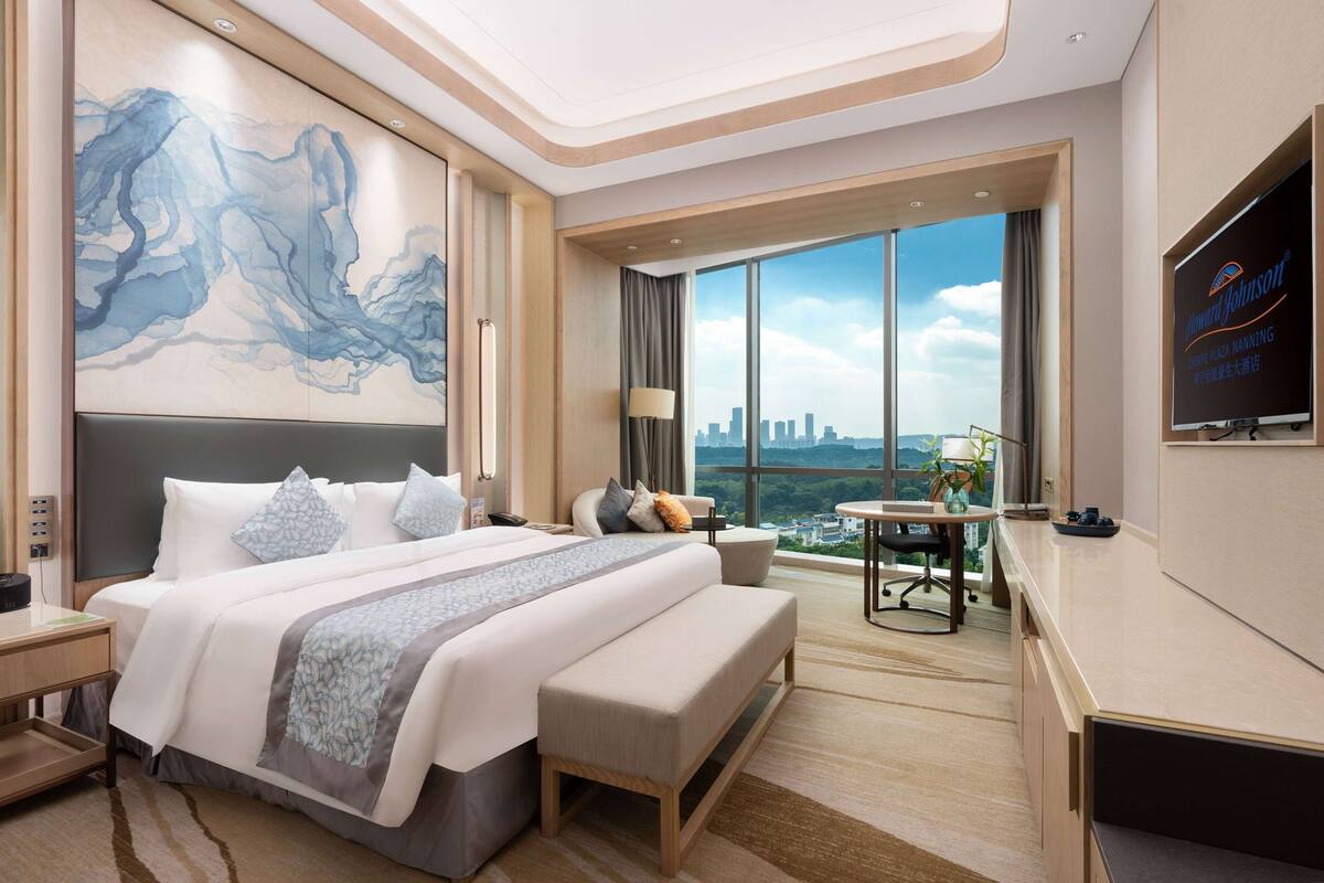 Una habitación de hotel moderna con una cama grande, un escritorio y vistas al horizonte de la ciudad.