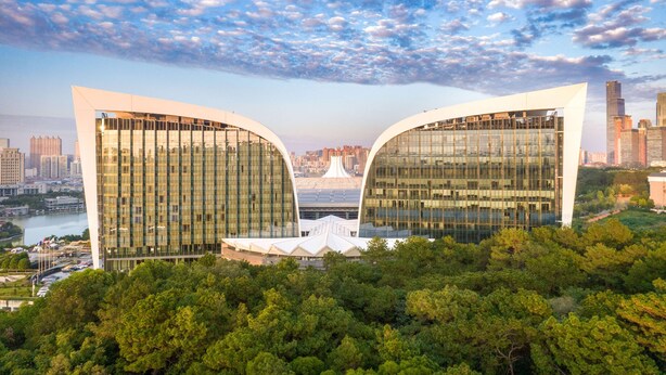 Un edificio moderno con un diseño curvo único, rodeado de exuberante vegetación y un río.