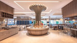 Un moderno vestíbulo de hotel con un mostrador de recepción central, zonas de estar y una gran lámpara decorativa.