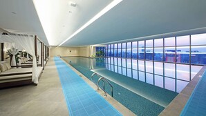Una piscina interior con vistas a la ciudad, una zona de estar con toldo y suelo de azulejos azules.