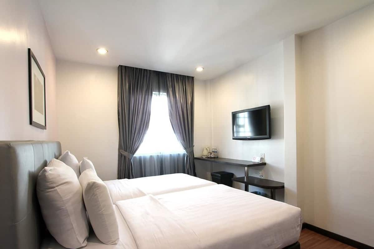 A hotel room with a large bed, a desk, a flat-screen TV, and a window with curtains.