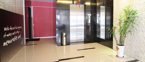 Un hall d’entrée moderne avec un mur d’accent rouge, un ascenseur en verre et une plante en pot.