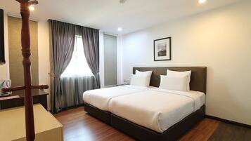 A hotel room with a large bed, a wooden floor, a desk with a chair, and a window with curtains.