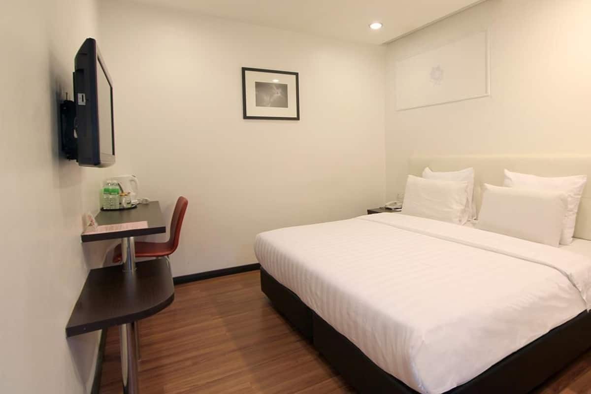 A hotel room with a bed, a desk with a chair, a TV mounted on the wall, and a framed picture on the wall.