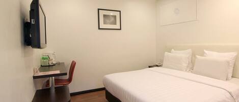 Habitación de hotel con cama, un escritorio con silla, televisor montado en la pared y un cuadro enmarcado.