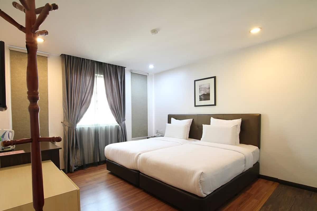 A hotel room with a bed, curtains, a bedside table, a picture on the wall, and a wooden floor.