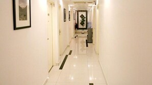 Ein Hotelgang mit weißen Wänden, gerahmten Kunstwerken und einem gefliesten Boden.