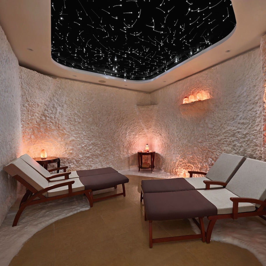 A spa room with stone walls, two lounge chairs, a small table, and a ceiling with a starry light display.
