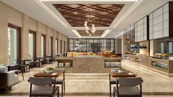 A spacious hotel lobby with a central seating area, a modern kitchen with a buffet, and large windows allowing natural light.