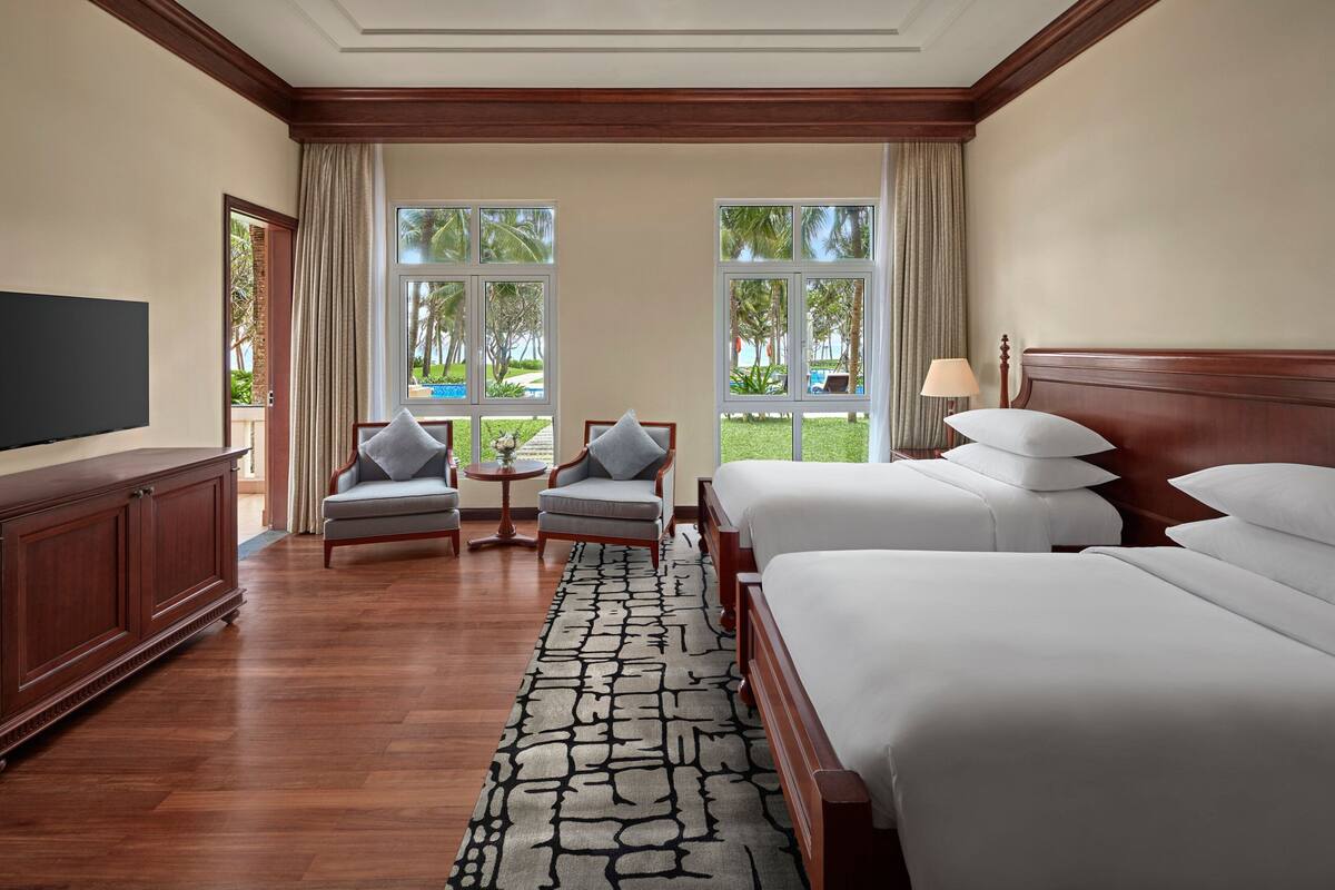 A hotel room with two beds, a TV, a wooden cabinet, a small table, and a chair.