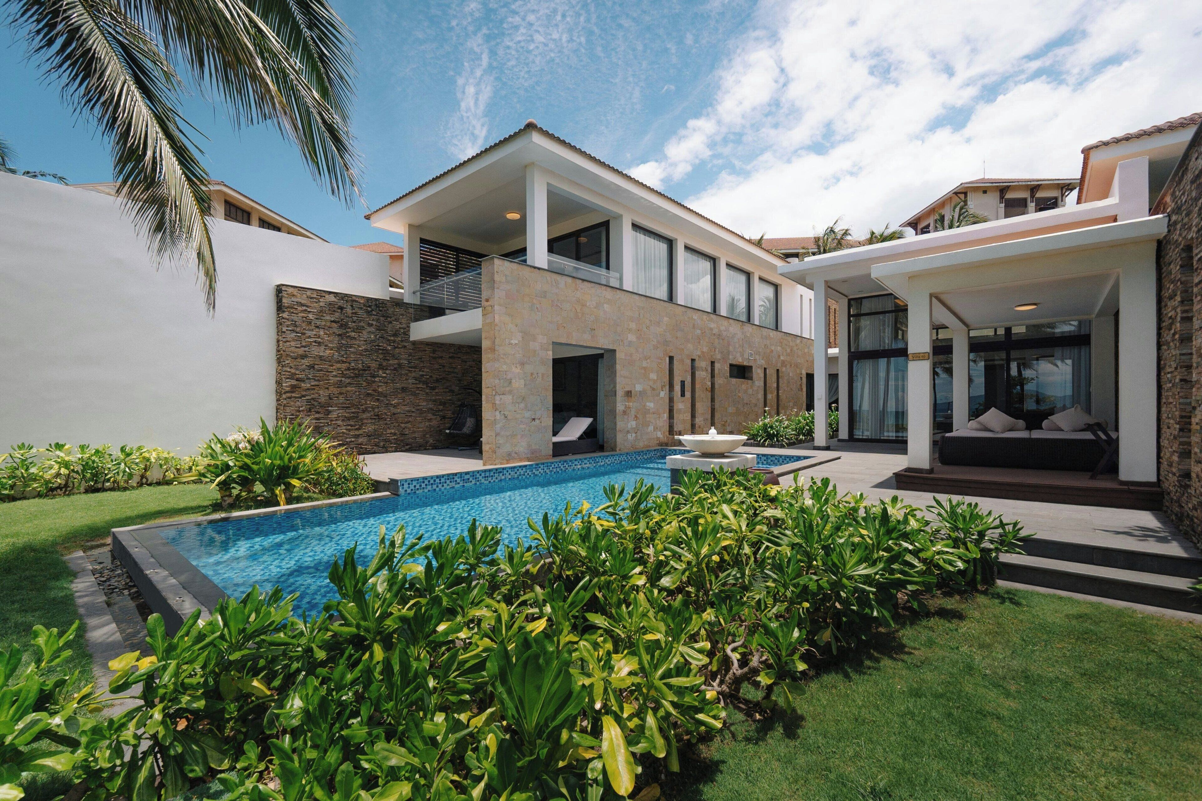 A modern house with a swimming pool, a stone facade, and a covered patio area.