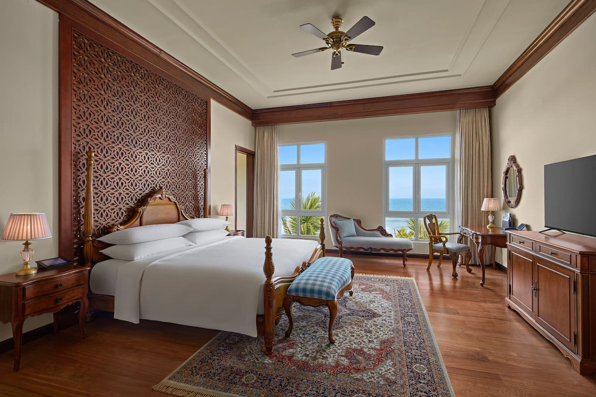 A spacious bedroom with a large bed, a sitting area with a view, and a television.