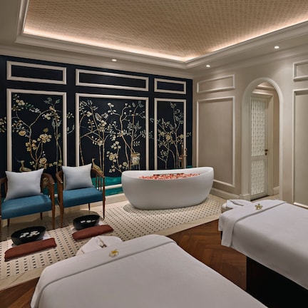 A spa room with two massage tables, a large bathtub, and a seating area with chairs and a bench.
