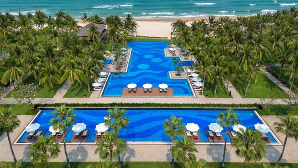 Un complexe hôtelier doté d’une piscine centrale, de palmiers et offrant une vue sur la plage.