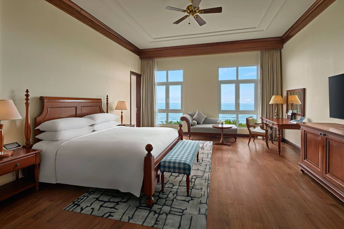 A hotel room with a large bed, a desk, a chair, a sofa, and a view of the ocean.
