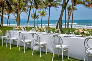 A long table set for a wedding with white chairs, a white tablecloth, and floral centerpieces.