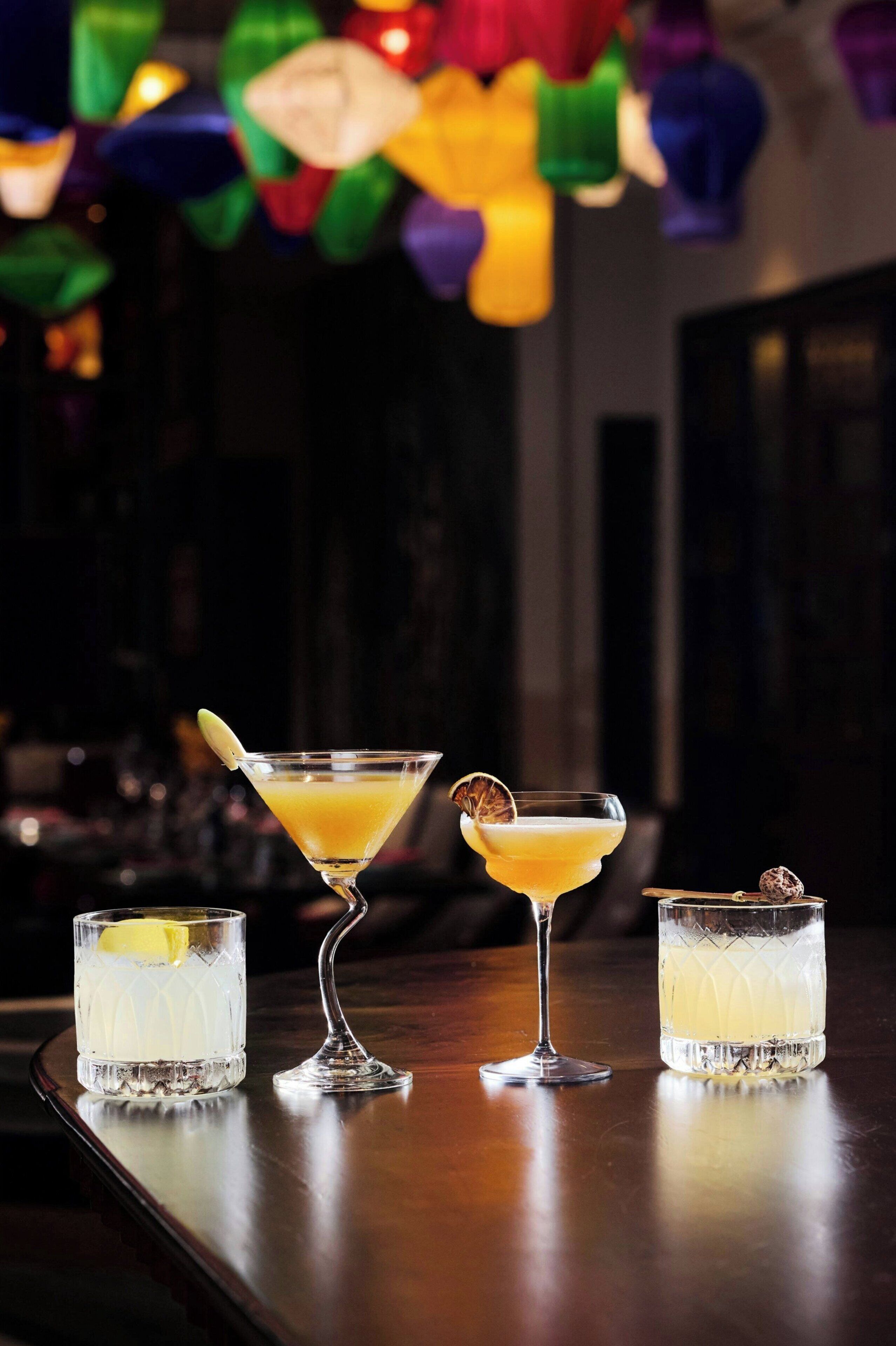 Three cocktails on a bar counter with a festive background.