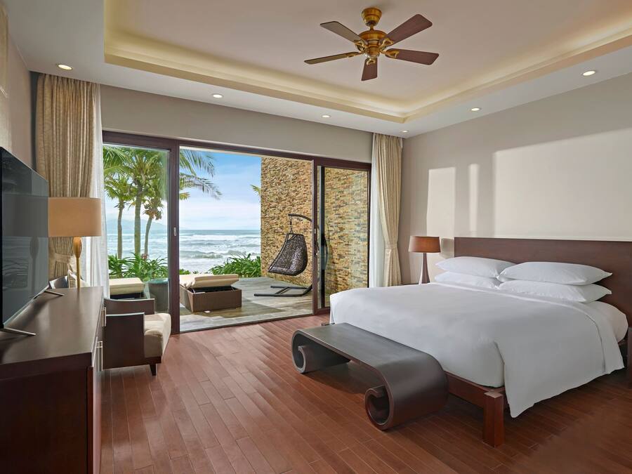 Habitación de hotel moderna con una cama grande, televisión, escritorio y vista al océano.