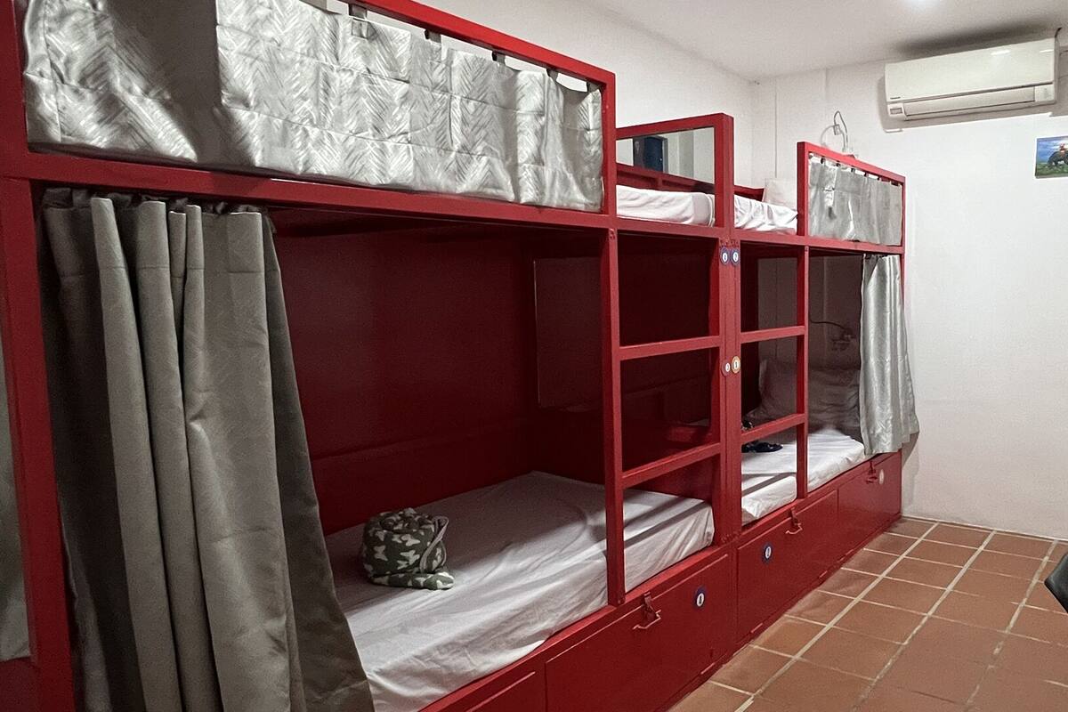 A dormitory room with bunk beds, a small table, and an air conditioning unit.