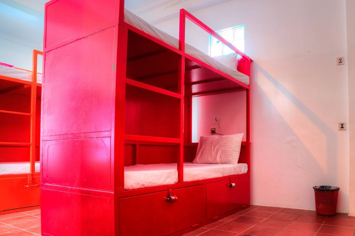 A room with red bunk beds, a small trash bin, and white walls.