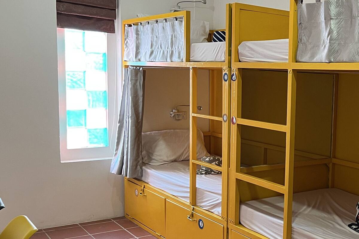 A bunk bed room with a window, curtains, and a chair.
