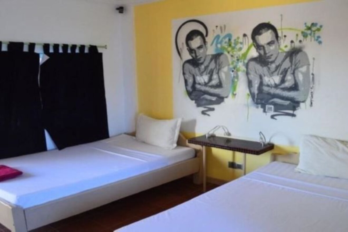 A room with two beds, a small table, and a wall with artwork.