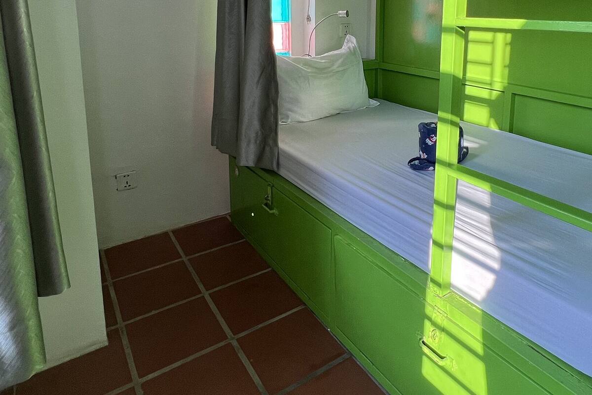A small, green-framed bed with a white mattress and a single pillow.